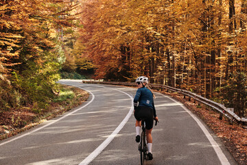 Woman cyclist rides a road bike through a scenic autumn forest. Vibrant fall foliage lines a winding road. Perfect for travel, sports, and nature themes. Transfăgărășan. Romania