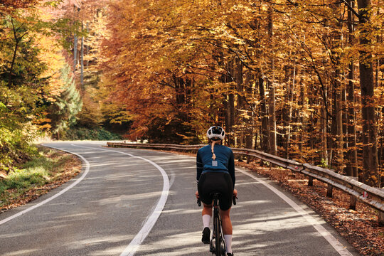 Woman cyclist rides through scenic autumn forest road. Golden leaves create vibrant background. Perfect for travel, sports, and nature themes.