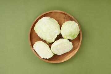 Green cabbage on a wooden plate, isolated against a green background, top view