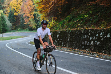 Obraz premium A cyclist enjoys a scenic autumn ride through a winding mountain road. The vibrant foliage provides a stunning backdrop to this active lifestyle image.