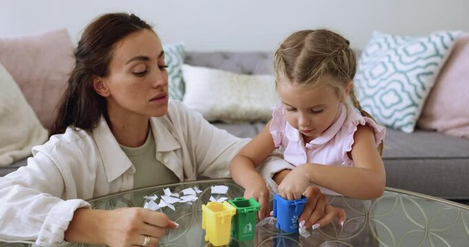 Loving mom teaching little kid to sort waste, playing recycling game with toy garbage and trash container, giving ecological education, caring for environment future, sustainable development