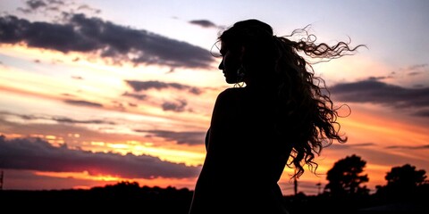 Fototapeta premium Silhouette of a Woman with Wavy Hair Captured from Behind, Emphasizing Elegant Hair Design Against a Dusk Sky, Creating a Stunning Contrast in Light and Shadow