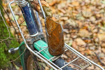 bottom of one dirty beer transparent round sharp dangerous broken old empty discarded brown bottle stands on iron rack of retro bicycle during daytime on street