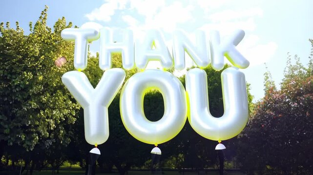 A large balloon sign that says "Thank You" in yellow letters. The sign is in a park with trees in the background