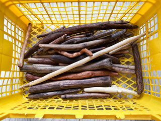 A variety of driftwood sticks in a bright yellow plastic container, showcasing natural textures and earthy hues. Perfect for themes of craftsmanship, resources, organization, or creative materials.
