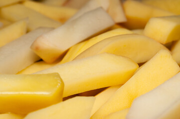 A close-up view of freshly cut, pale yellow potato wedges piled together