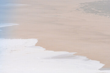Soft white waves breaking gently onto a vast sandy beach in Nazare, Portugal