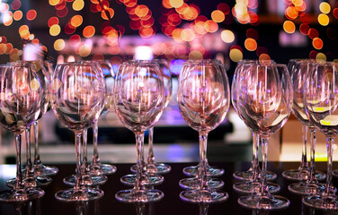 Elegant wine glasses arranged on a table at a festive evening gathering with colorful lights in the background