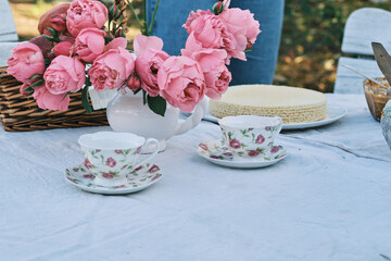 Elegant outdoor tea party scene with pink roses, delicate teacups, and a waffle cake. Perfect for blogs, websites, or publications focused on lifestyle,  food, or events.