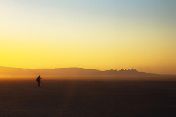 Fototapeta premium At sunrise and sunset in the vast expanse of Wadi Rum, people engage in various activities, surrounded by the enchanting beauty of the desert. The golden hour casts a warm glow over the hazy landscape