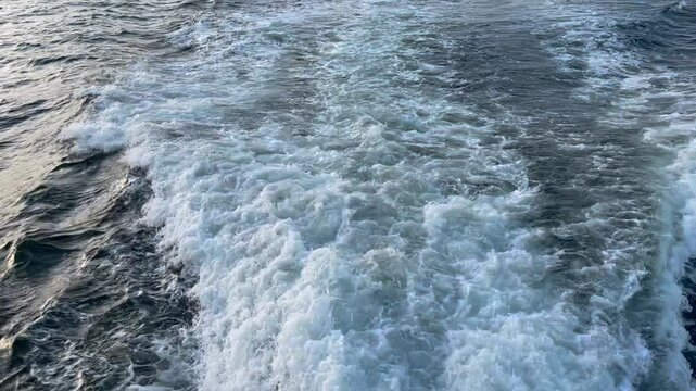 Big waves on water surface with white foam from moving ship in ocean 