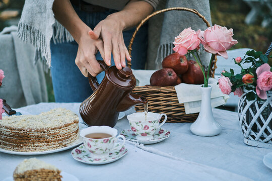 Woman pouring tea at an outdoor picnic with cake and roses. Enjoy the cozy autumn atmosphere. Perfect for blogs, websites, or social media.