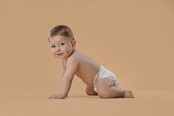 Cute little baby in diaper crawling on beige background