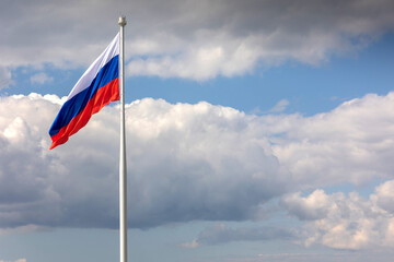 Flag of Russian Federation is flying in air on blue sky and white cumulus clouds. National flag of Russian.