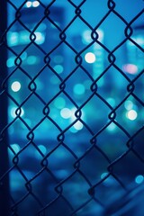 Naklejka premium Urban night view through chain link fence with blurred city lights in the background