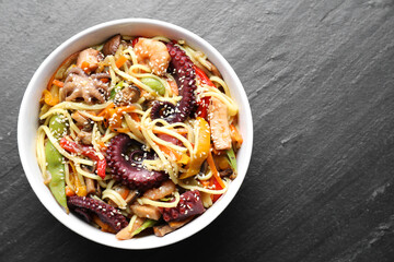 Stir-fry noodles with sea food in bowl on grey textured table, top view. Space for text