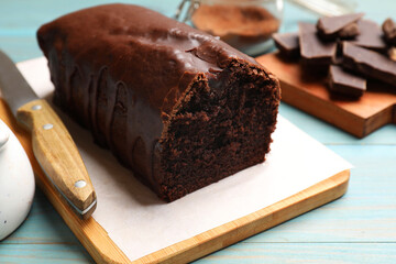 Tasty chocolate sponge cake on light blue wooden table, closeup
