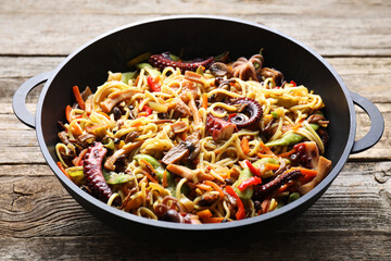 Stir-fry noodles with sea food and vegetables in wok on wooden table, closeup