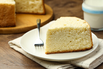 Piece of delicious sponge cake and fork on wooden table, closeup