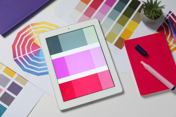 Designer's workplace with tablet, different palettes and stationery on white table, flat lay