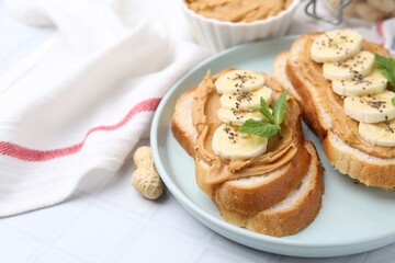 Tasty sandwiches with peanut butter, banana, chia seeds and mint on white table, closeup