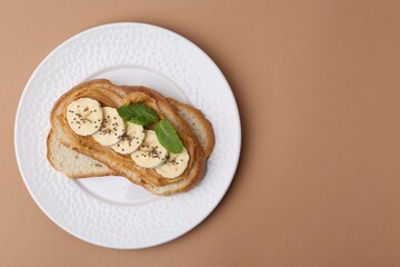 Tasty sandwich with peanut butter, banana, chia seeds and mint on brown background, top view. Space for text