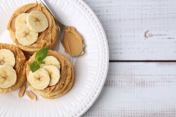 Tasty sandwiches with peanut butter, banana, mint and spoon on white wooden table, top view. Space for text
