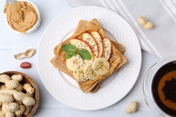 Tasty sandwich with peanut butter, apple, banana, chia seeds, nuts and mint on white table, flat lay