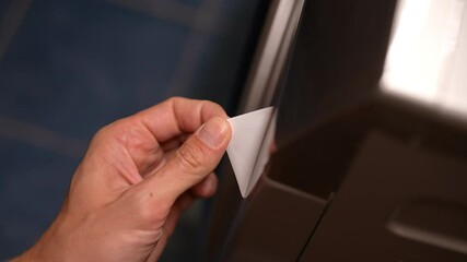 Close-up of male hand carefully peeling sticker from shiny surface of new washing machine. Process of removing protective film from household appliances, closeup, unrecognizable person, slow motion.