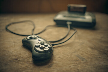 A wired gamepad joystick with a black game console on a wooden table.Console games of the 90s. © Svetliy