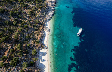 Drone Aerial view of tourists enjoying summer on a Greek isolated tropical beach with turquoise water.