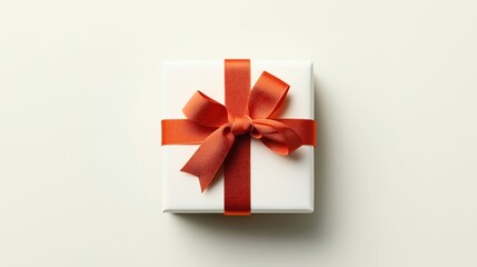 Square white gift box with a large red ribbon and bow on a light-colored background, viewed from above, emphasizing simplicity and elegance in presentation.