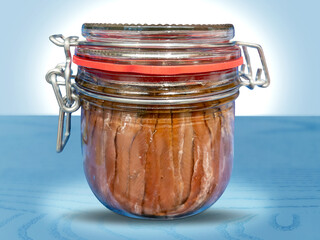 Anchovy fillets in olive oil in glass jar with hermetic spring closure on a blue table