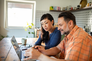 Couple managing bills with laptop on kitchen desk at home