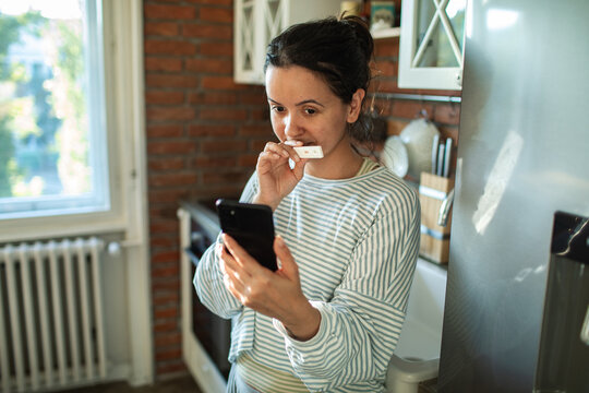 Young woman showing positive pregnancy test to a smartphone in kitchen