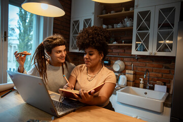 Two young women collaborating at home with a laptop and notebook