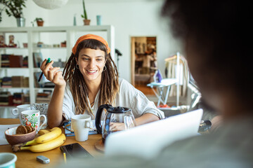 Young woman with dreadlocks studying at a table with friends and coffee cups