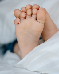The feet of a small child in a parent's bed on white sheets rolled in a white blanket  
