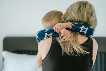 son in his pajamas in the morning hugs his mom hard around the neck. 