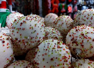 White colored Christmas baubles  with green and red speckles are on a store shelf during a Christmas show in a shop and are ready to be sold before the start of the holiday season