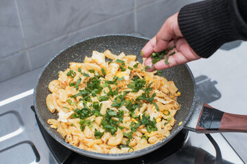 A closeup of a women hand cooking the pasta macaroni or penne pasta in wok pan, pouring spring onions and celery to the pasta macaroni or penne pasta in pan,  cooking pasta homemade.