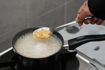 A women cooking the pasta macaroni or penne pasta in wok pan pot in boiling water, cooking pasta homemade.