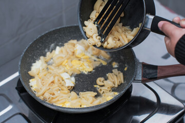 A closeup of a women hand cooking the pasta macaroni or penne pasta in wok pan, pouring the pasta macaroni or penne pasta to pan,  cooking pasta homemade.