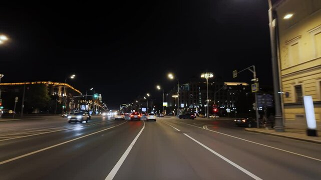 Driving a car in summer night illuminated city streets, windshield view