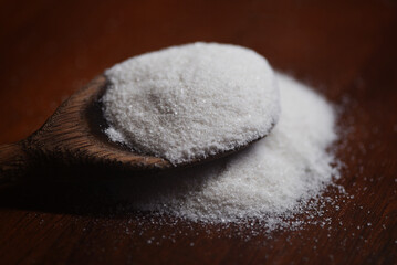 White refined salt. Salt handled with a wooden spoon. Sodium chloride, known as salt or table salt, important food preservative and popular seasoning.