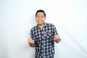 cheerful asian man raising fist showing winning and success gesture expression wearing casual shirt isolated on white