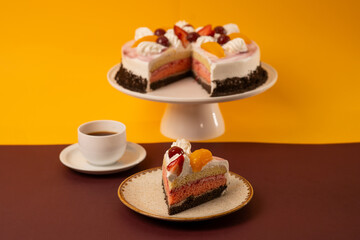 Delicious Slice of Cake Topped with Fresh Fruits and Cream with coffee cup on yellow and brown background