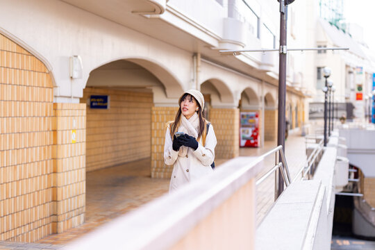 Asian woman using navigation online map on smartphone with internet during walking on city street in Tokyo, Japan. Attractive girl enjoy outdoor lifestyle travel in the city on winter holiday vacation