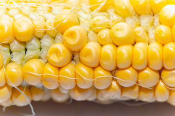 Corn cob highlighting the individual kernels. The kernels are yellow and appear plump and juicy, with some corn silk visible between them. Detailed look at the texture and arrangement of corn kernels