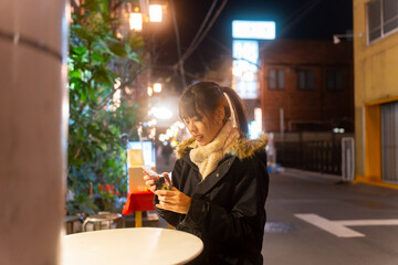 Young Asian woman eating caramel pudding during travel Asakusa district, Tokyo, Japan at night. Attractive girl tourist travel Japan landmark and walking city street market in winter holiday vacation.